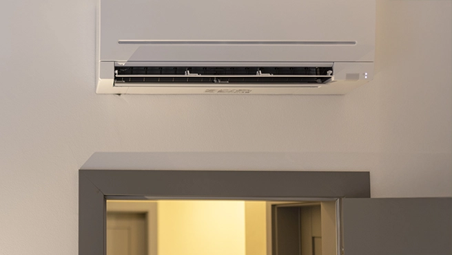 Wall-mounted air conditioning unit above a door in a room.