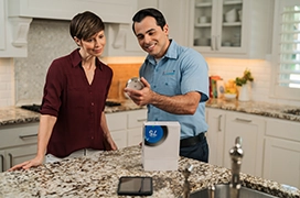 Aire Serv tech showing thermostat to customer in kitchen.