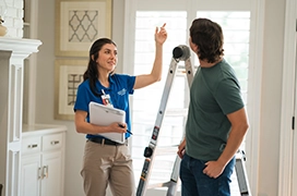 Woman pointing to ceiling talking to Aire Serv tech with ladder.