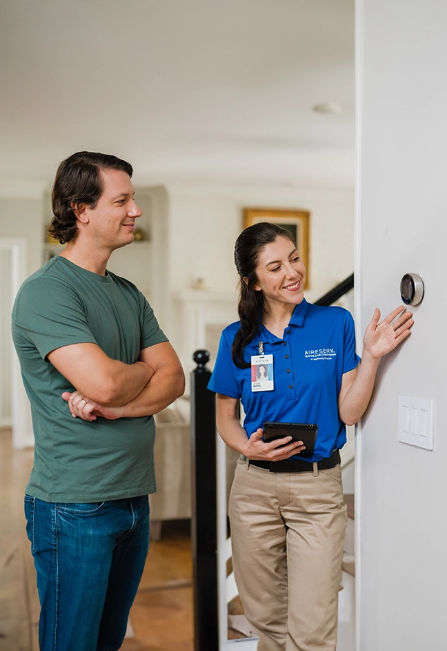 Aire Serv female tech explaining thermostat to male customer.