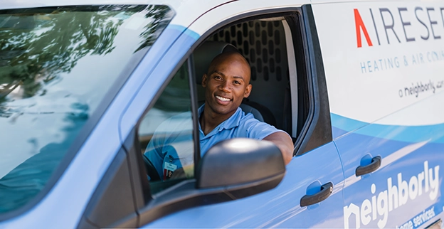 Aire Serv technician smiling from the driver's seat of an Aire Serv van.