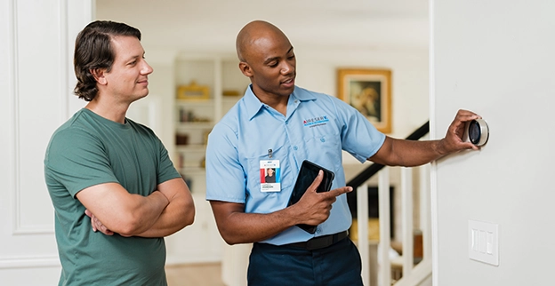 Aire Serv technician showing a client a thermostat installed on the wall.