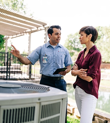 Aire Serv tech talking with female customer outside about HVAC system.