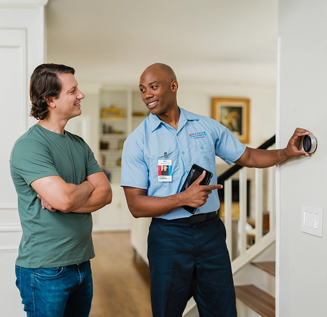 Aire Serv technician showing a customer a thermostat installed on their wall.