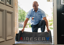 An Aire Serv technician laying out a branded doormat in front of a customer's door.