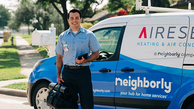 Aire Serv tech carrying bag in front of branded van.