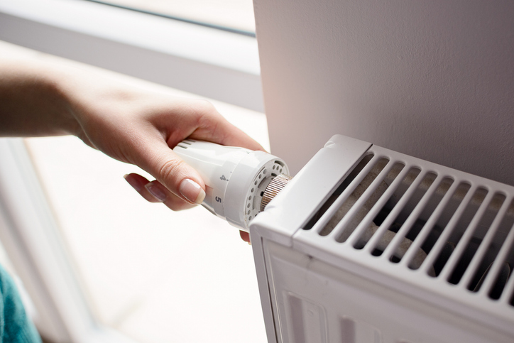 A close-up of a person&rsquo;s hand adjusting the thermostat valve knob on the side of a radiator. | Aire Serve of North Central Arizona