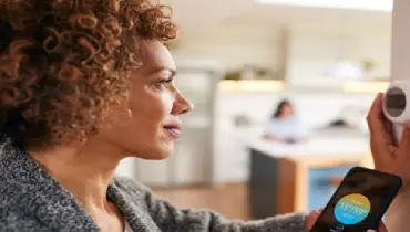 Mature woman using app on phone to set temperature on smart thermostat in home.