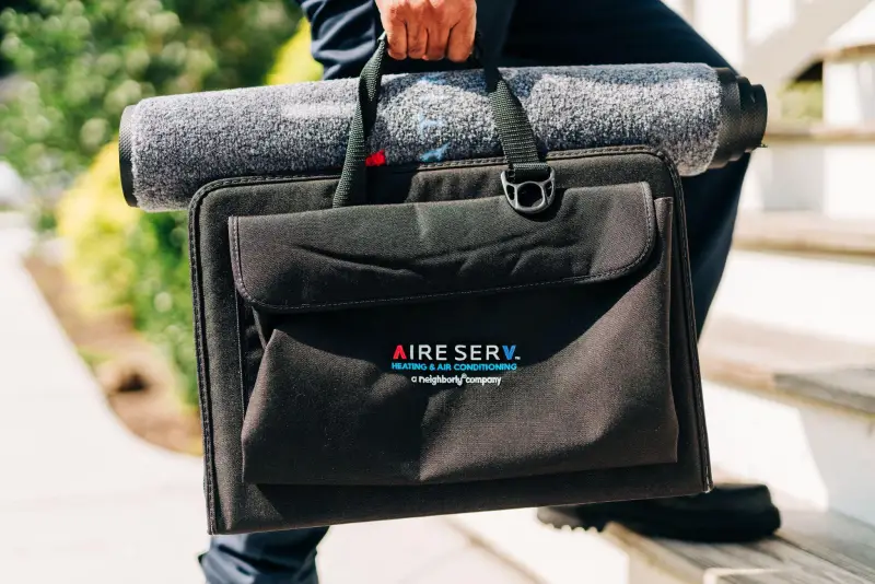 HVAC repair person carries a toolbag into a home.