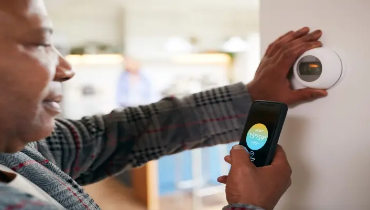 Man using smartphone with thermostat app displayed on screen.