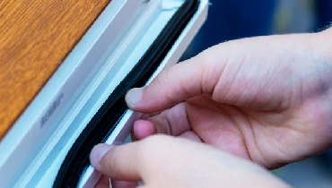 Person applying weather stripping to a window frame