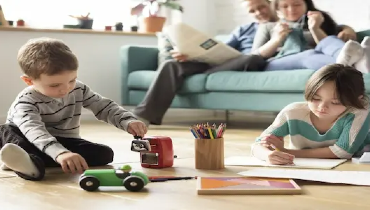 Young children playing in living room with parents relaxing on couch.