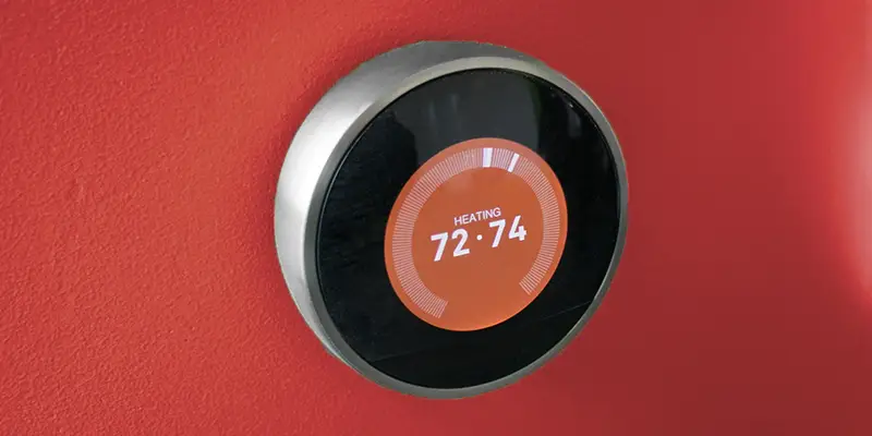 Smart thermostat on dark orange wall reading 72-74