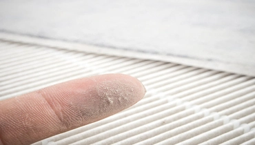 Dust on finger with air filter in background.