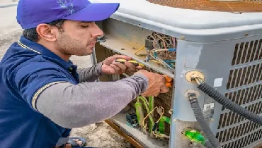 A professional technician fixing a heavy air conditioner with his tools and wearing blue color uniform and cap.