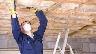 Man wearing a mask putting insulation in a ceiling