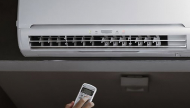 Air conditioner on wall with a hand pointing a remote at it