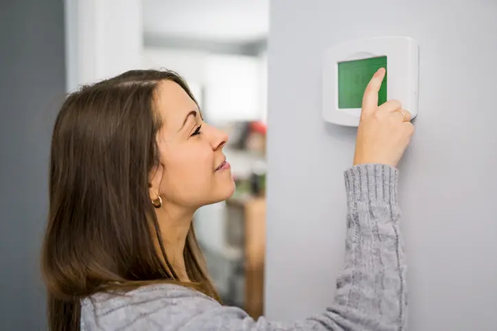 A woman is seen using a thermostat in her home. | Aire Serv® of Jackson