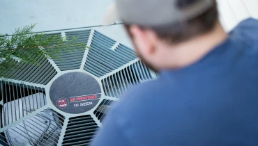 Overhead view of a man looking into the top of an air conditioning unit. 