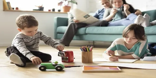 Young children playing in living room with parents relaxing on couch.
